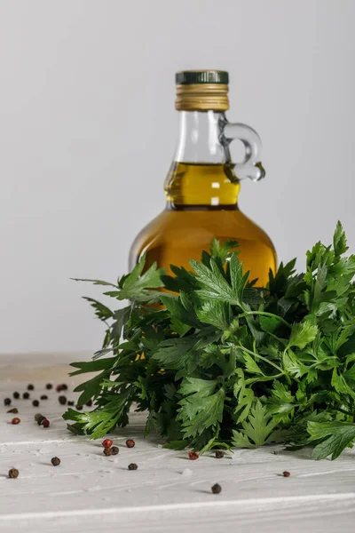 Bottle of oil near cilantro bung and scattered red and black peppercorns on white wooden table isolated on grey — Stock Photo