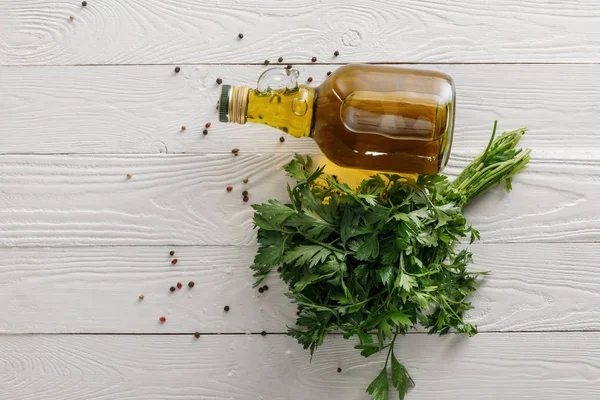 Top view of bottle of oil near fresh cilantro bung and peppercorns on white wooden surface — Stock Photo