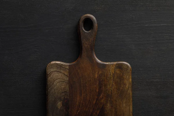 Top view of brown wooden cutting board on dark surface — Stock Photo