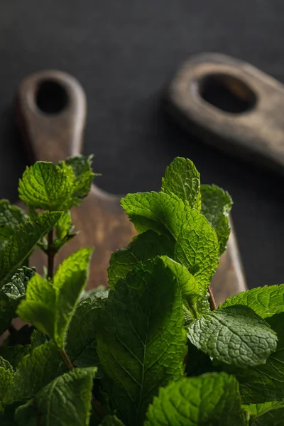 Fresh peppermint twigs near brown wooden cutting boards on dark surface — Stock Photo