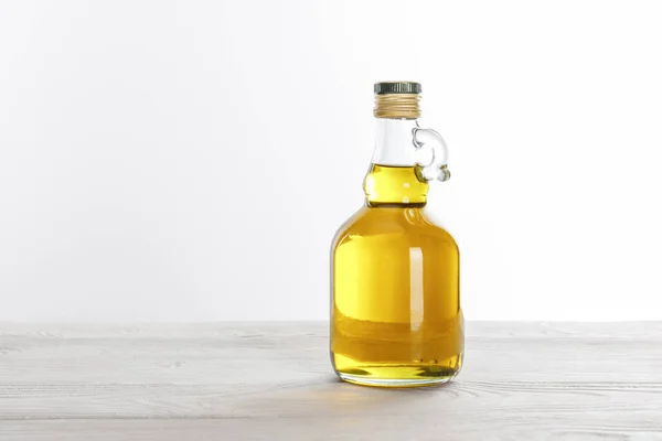 Transparent glass bottle of oil on white wooden table isolated on white — Stock Photo