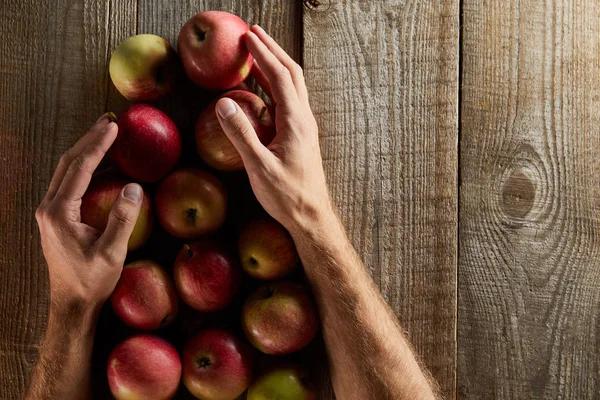 Vue recadrée de l'homme tenant des pommes ow surface en bois — Photo de stock