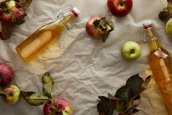 Draufsicht auf Flaschen mit Apfelwein in der Nähe verstreuter Äpfel und Blätter — Stockfoto