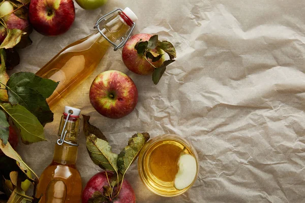 Top view of bottles and glass with cider near scattered apples with copy space — Stock Photo