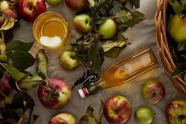 Vue du dessus de la bouteille et du verre avec du cidre près des pommes et du panier en osier — Photo de stock