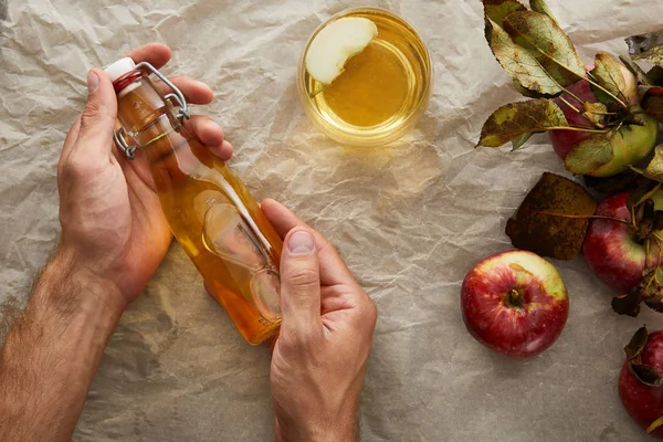 Cropped image of man holding bottle of apple cider under parchment paper with apple and glass — Stock Photo