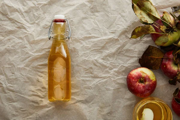 Vue du dessus du papier parchemin avec pommes fraîches, bouteille et verre de cidre avec espace de copie — Photo de stock