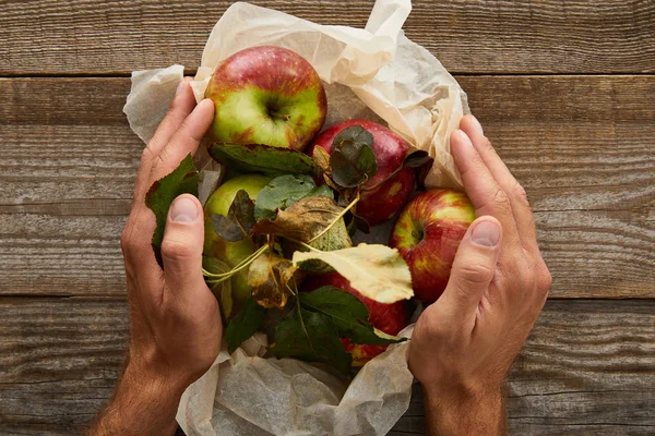 Imagen recortada del hombre sosteniendo papel pergamino con manzanas en la superficie de madera - foto de stock