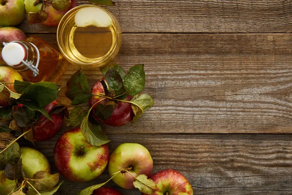 Vista superior de manzanas maduras cerca de botella y vaso de sidra fresca en superficie de madera - foto de stock