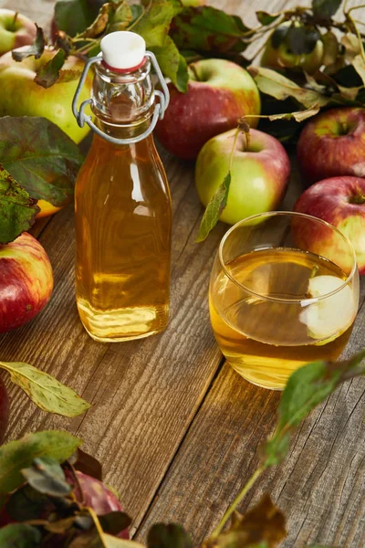 Bottiglia e bicchiere di sidro fresco su superficie di legno con mele mature — Foto stock