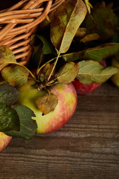 Close up view of ripe apples near wicker basket on brown wooden surface — Stock Photo