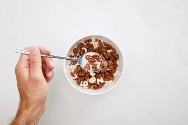 Imagen recortada del hombre tomando cereal con cuchara del tazón en la superficie de mármol - foto de stock