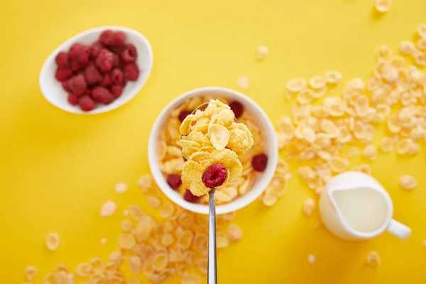 Top view of spoon with cornflakes and fresh raspberry above bowl with breakfast isolated on yellow — Stock Photo