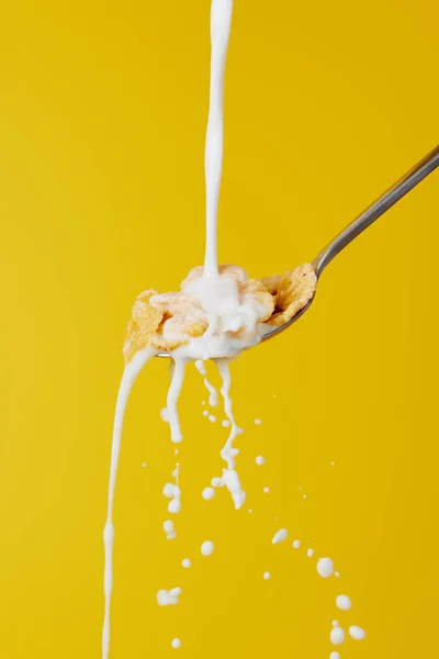 Cuchara con copos de maíz y chorro de leche con salpicaduras aisladas en amarillo - foto de stock