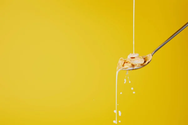 Cuchara con copos de maíz y torrente de leche aislado en amarillo — Stock Photo