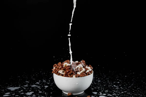 Tazón blanco con surtido de cereales con salpicaduras de leche aisladas en negro - foto de stock