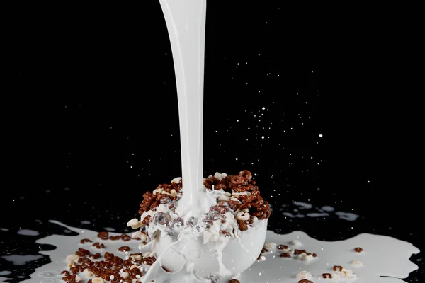 Tigela branca com cereal sortido com poderosa corrente de leite isolado em preto — Fotografia de Stock