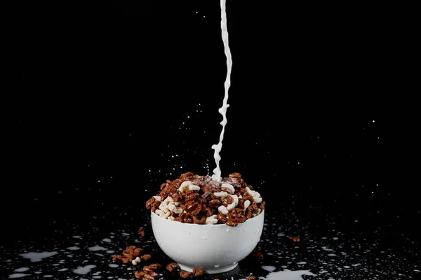 Tazón blanco con surtido de cereales con chorro de leche y salpicaduras aisladas en negro - foto de stock