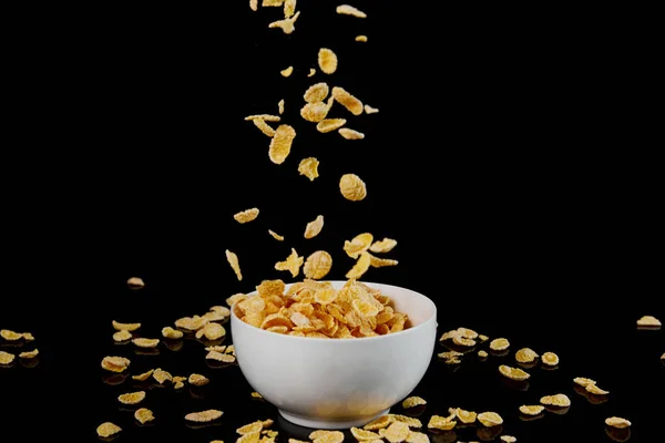 White bowl with cornflakes and fallen pieces isolated on black — Stock Photo