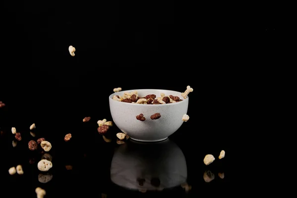 White bowl with cereal and fallen pieces isolated on black — Stock Photo