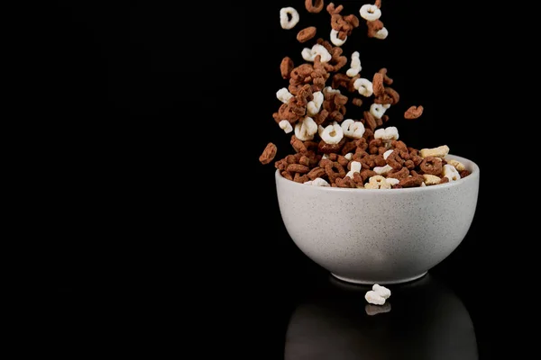 Tazón blanco con trozos de cereal caídos aislados en negro - foto de stock