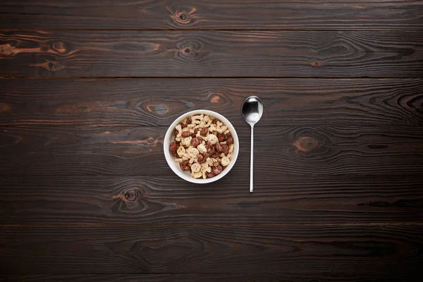 Vista superior de la cuchara cerca del cereal en un tazón sobre una superficie de madera - foto de stock