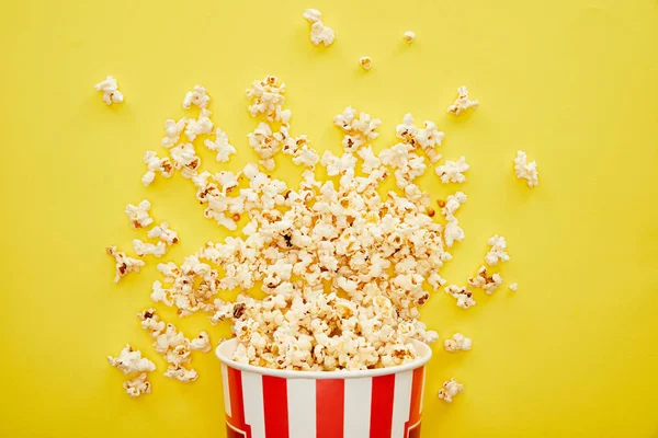 Vue du dessus de délicieux pop-corn éparpillés dans un seau rayé sur fond jaune — Photo de stock