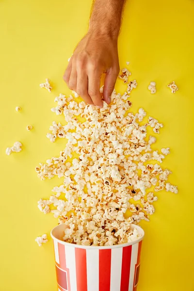 Cropped view of man taking delicious popcorn from bucket on yellow background — Stock Photo
