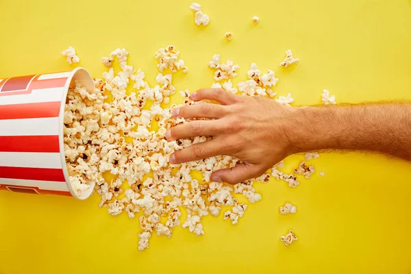 Abgeschnittene Ansicht eines Mannes, der die Hand auf leckeres Popcorn auf gelbem Hintergrund legt — Stockfoto