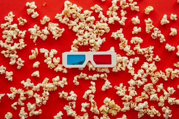 Top view of 3d glasses on scattered popcorn on red background — Stock Photo
