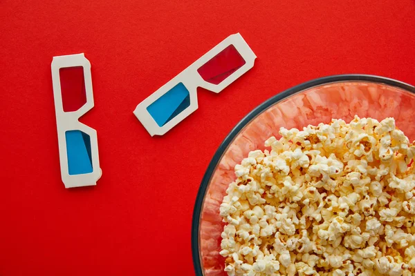 Draufsicht auf köstliches Popcorn in Schüssel in der Nähe von 3D-Gläsern isoliert auf Rot — Stockfoto