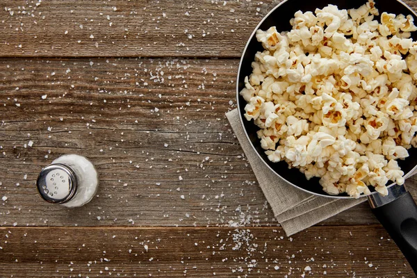 Top view of fresh popcorn in frying pan with salt on wooden background — Stock Photo