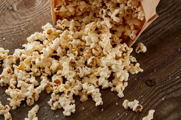 Délicieux pop-corn croustillant dispersé du sac en papier sur fond en bois — Photo de stock