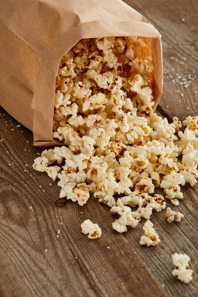 Salziges, köstliches Popcorn aus Papiertüte auf Holzoberfläche verstreut — Stockfoto