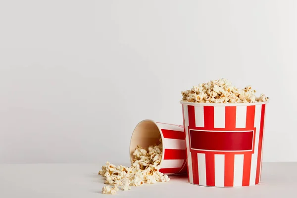 Tasty popcorn scattered from red striped paper buckets isolated on grey — Stock Photo