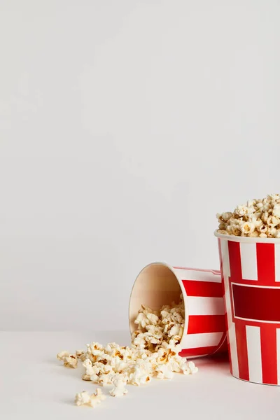 Popcorn scattered from red striped paper buckets isolated on grey — Stock Photo