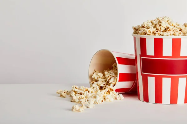 Deliziosi popcorn sparsi da secchi di carta a strisce rosse isolati su grigio — Foto stock
