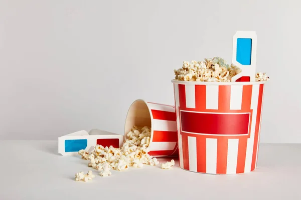 Leckeres Popcorn in gestreiften Eimern mit 3D-Gläsern isoliert auf grau — Stockfoto