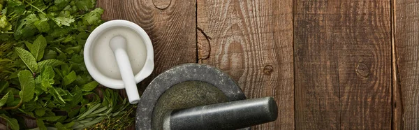 Panoramic shot of white and grey mortars with pestles on wooden surface with fresh herbs — Stock Photo