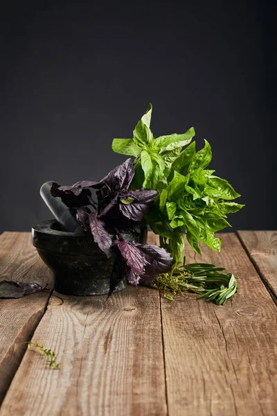 Mortar with fresh green and purple basil with rosemary on wooden table isolated on black — Stock Photo