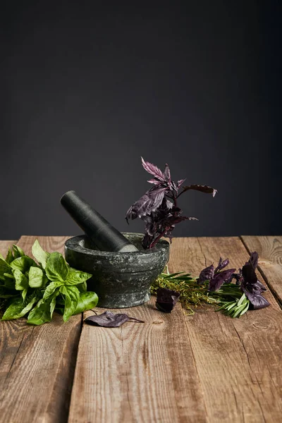 Mortier gris avec pilon près de basilic vert frais et violet sur table en bois isolé sur fond noir — Photo de stock