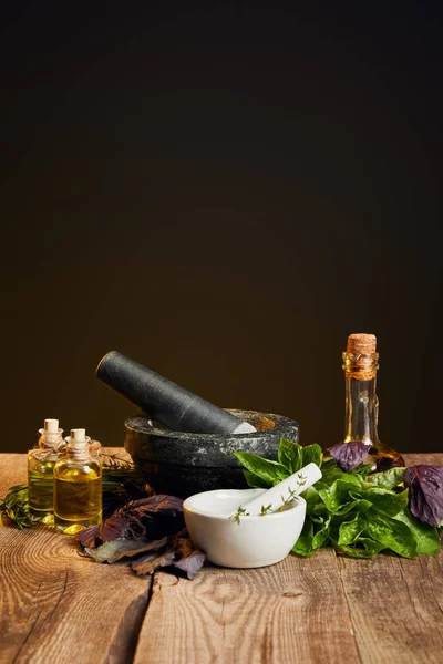 Mortai con pestelli e bottiglie con olio vicino erbe fresche su tavolo di legno isolato su nero — Foto stock