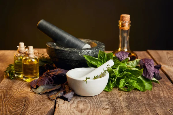 Mörser mit Stößeln und Flaschen in der Nähe von frischen Kräutern auf Holztisch isoliert auf schwarz — Stockfoto