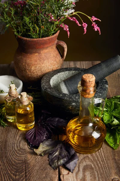 Mortar with pestle, bottles with oil and clay vase with fresh wildflowers on wooden surface isolated on black — Stock Photo