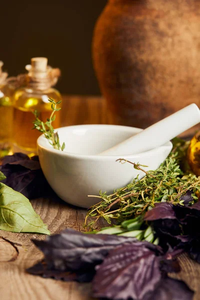 White mortar with pestle near bottle with oil and fresh herbs on wooden surface isolated on black — Stock Photo