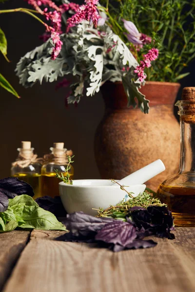 Mörser mit Stößel in der Nähe von Flaschen mit Öl und Vase mit frischen Blumen auf hölzerner Oberfläche isoliert auf schwarz — Stockfoto