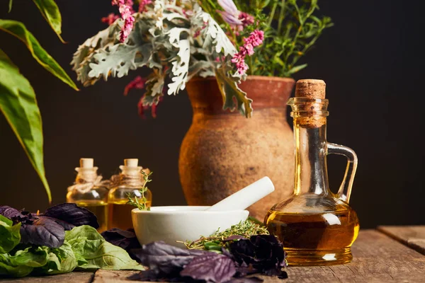 Mortero blanco con mortero cerca de botellas de aceite y jarrón con flores frescas en la superficie de madera aislado en negro - foto de stock