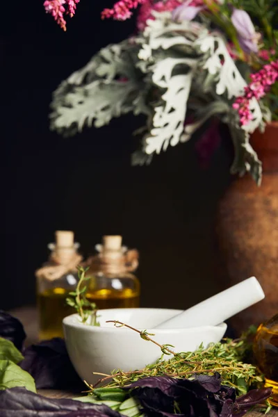 White mortar with pestle near bottles and vase with fresh flowers on wooden surface isolated on black — Stock Photo