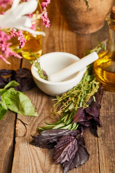 Mortar with pestle near bottles and fresh leaves and flowers on wooden surface — Stock Photo