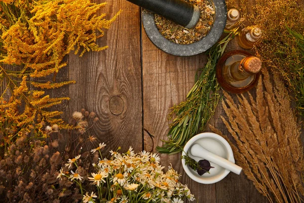 Top view of mortars with pestles with herbal mix near wildflowers on wooden surface with copy space — Stock Photo